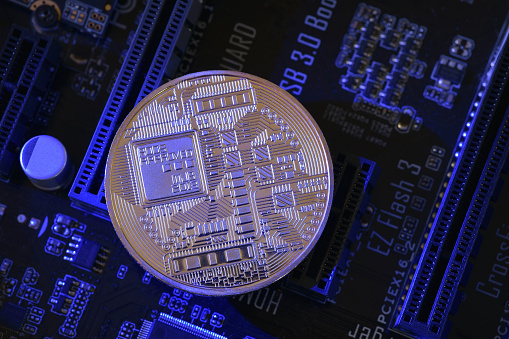 Photograph of souvenir Bitcoin coin back side on motherboard. Decentralised digital currency that relies on peer-to-peer software and cryptography.  Bitcoin mining is the process new coins are entered into circulation by solving  math problems,  transactions are verified on the blockchain. Bitcoin halving event.