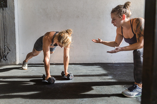 Two female athletes focus on their fitness goals as they lift dumbbells together.