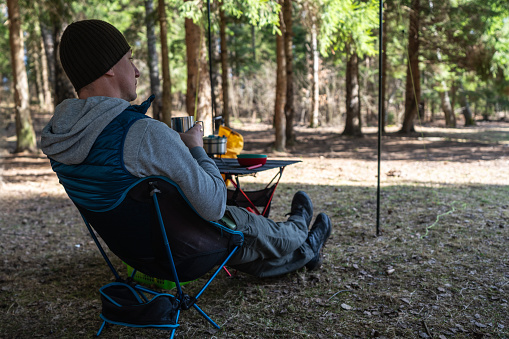 A man sitting on the foldable touristic chair at the campsite in the woods