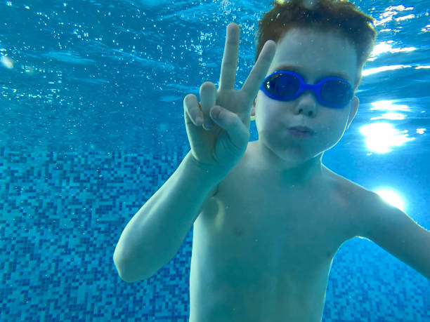 a boy showing peace or victory sign underwater in the pool - mobilestock freedom enjoyment blue стоковые фото и изображения