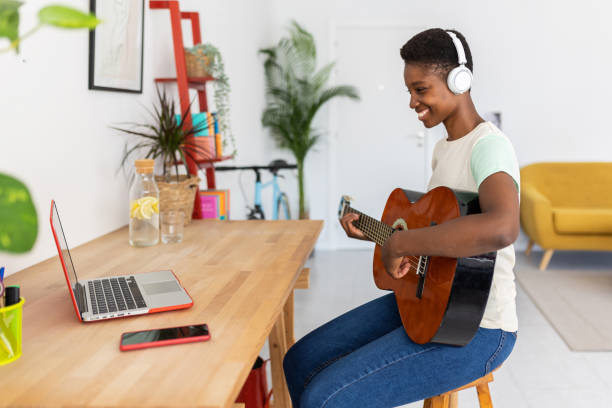 istock Smiling young african woman playing acoustic guitar while watching online course 1992424445