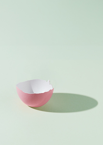 Half of a pink eggshell on a green background with a shadow of the whole egg. Easter minimal abstract concept. Upright rectangle with copy space