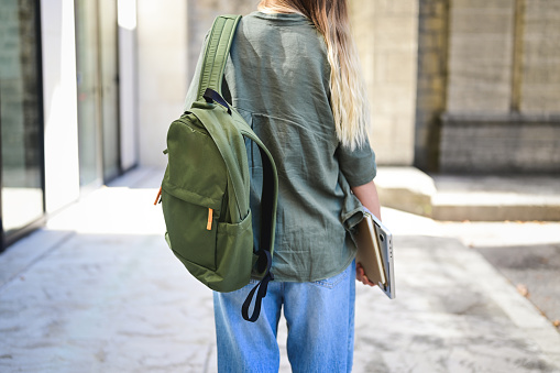 Rear view of a modern woman with backpack and laptop outdoors.