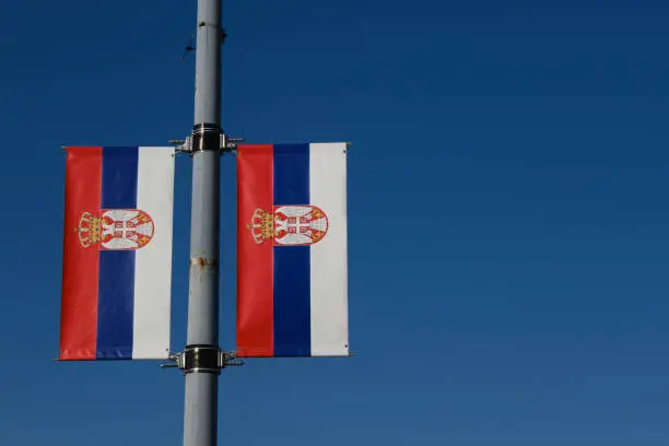 Photo of Serbian flags against the blue sky on a sunny day in the center of Belgrade. Red blue white tricolor with the symbol of the coat of arms of Serbia. Patriotic concept, background with copy space.