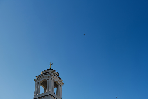 The dome of the chapel with a bell inside and a cross on the roof. A quadcopter and birds fly over the church on a sunny day. Shooting photos and video content from the air using modern technology