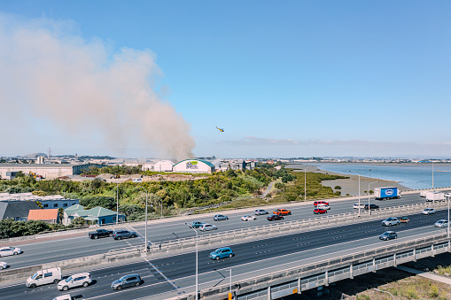 Fire sets out at a waste facility of Green Gorilla producing smoke on 7th February 2024 in Onehunga, Auckland. Fire fighters try extinguishing from the ground and the air, with the helicopters dumping water