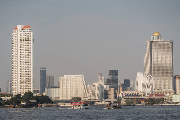 A serene view of Bangkok skyline and bustling Chao Phraya River with boats and high-rises.