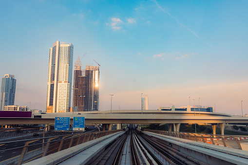 Looking out of the metro train to the dramatic sunset over modern skyscrapers  and the multilane highway road in Dubai, United Arab Emirates