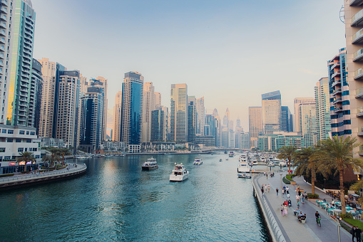 Dubai Marina city skyline with pedestrian road, modern buildings and group of yachts on the water in United Arab Emirates