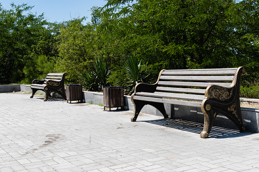 Two comfortable wooden benches for relaxing on observation deck. Near benches there are garbage cans stylized with wood. Metal structures are painted in gold.
