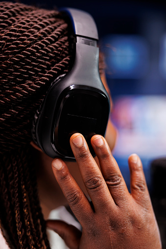 Selective focus on black individual wearing wireless headphones, listening to online comments from talk show audience. Closeup of african american woman using headset when recording a podcast.