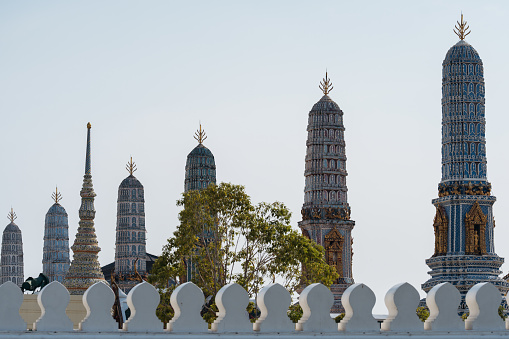 Scenic view of ornate Thai temple spires rising behind a curving white fence.
