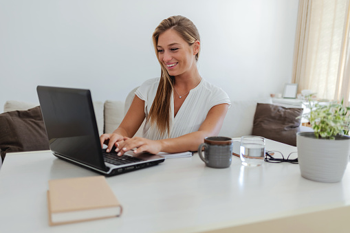 Elegant, professional and freelance worker on her laptop inside home office. Formal, stylish and fashionable corporate employee online. Remote, communication and sending emails in digital workplace.