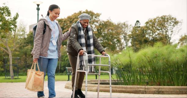 nurse, support and walker with old woman in park for helping, person with a disability and retirement. elderly care, nursing and rehabilitation with caregiver and patient in nature for healthcare - ouderenzorg stockfoto's en -beelden