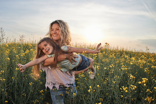 Young mother and daughter in field on a sunset. Single mother is carrying little girl.