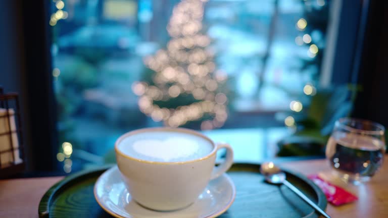 Cup of coffee with foam latte art in heart shape. Christmas tree on background