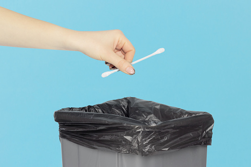 throw a cotton swab, ear swab in the trash bin, ear swab in hand in front of the trash bin, hygiene products recycling concept