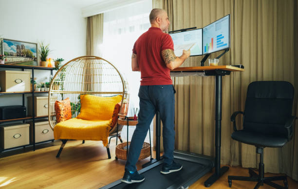 istock Man working from home at standing desk is walking on under desk treadmill 1992649589