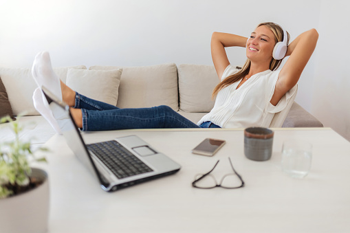 Young businesswoman listening to the music and relaxing at home. Positive happy young woman enjoy music through headphones while working freelance work at home.