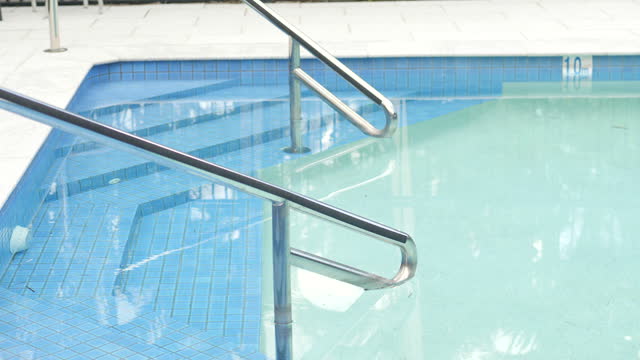 Steps and hand rails leading into a swimming pool with ripples and reflections of the surface clear cool water