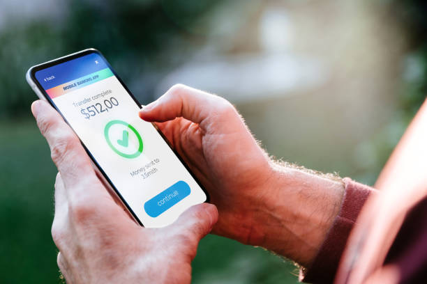 istock Man making money transfers online using apps to send and receive currency. Mobile phone with a financial application on screen. Money transfer concept. 1992681259