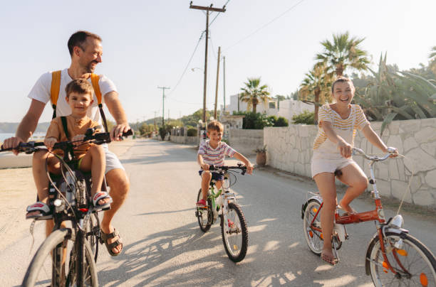 Photo of a young family, with two little boys, enjoy beautiful summer morning riding bicycles by the sea