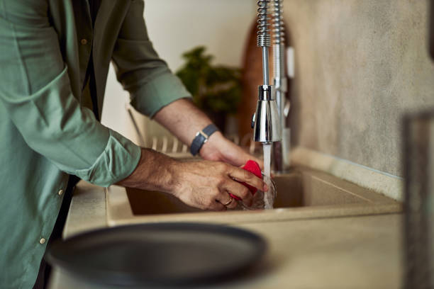 istock A man washing dishes in the kitchen sink in the kitchen, using a red cleaning sponge. 1992709346