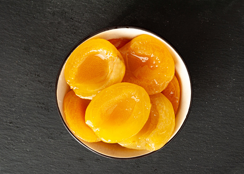 Canned Peaches in Bowl, Apricot Halves in Syrup, Yellow Fruit Dessert, Tinned Nectarine Compote, Orange Peeled Peache Slices on Black Background