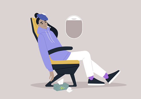 A young adult sick with flu and fever in the airplane chair, an ice bag resting on their forehead
