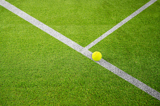 Closeup of one yellow tennis ball or paddle tennis and white lines on green court. Horizontal sport poster, greeting cards, headers, website
