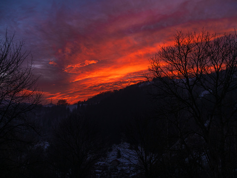 Sunset in the mountains with orange red sky and clouds. Winter Carpathian Mountains view cloudscape. Pine fir tree forest in Carpathians Scenic wood landscape Village in Transcarpathia Ukraine, Europe