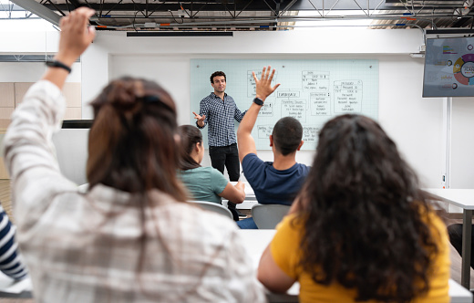 Young teacher standing near the blackboard and explaining material to students at lesson in the classroom