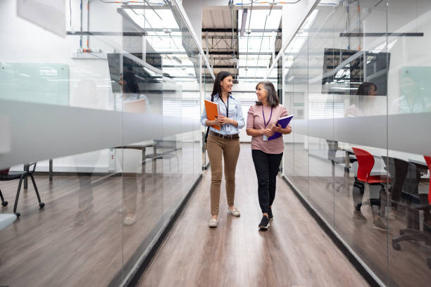 Happy female teachers talking in the hall at the university Happy female teachers talking in the hall at the university while walking towards the classroom - education concepts coaching stock pictures, royalty-free photos & images