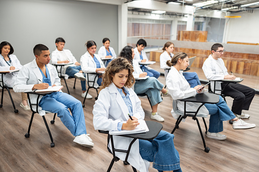 Group of Latin American medical students taking notes in class while listening to a lecture - medical school concepts