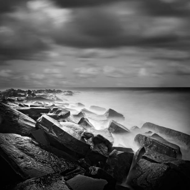 a black and white photograph, taken using long exposure technique, depicting the square-shaped rocks submerged in the sea. stock photo - black and white landscape square long exposure стоковые фото и изображения