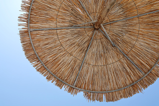 Close up wicker sunshade with blue sky backdrop.