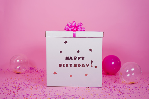 Big cardboard box birthday surprise and balloons with confetti on pink background