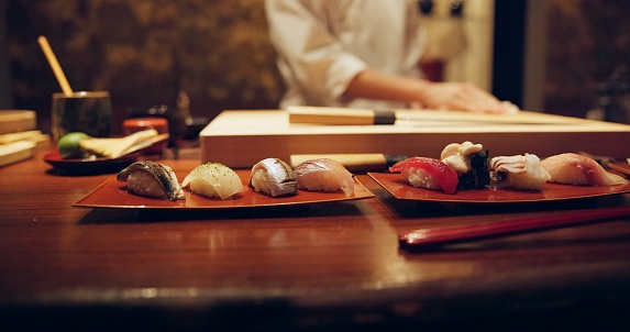 Sushi, plate and serving with chef in restaurant for luxury cuisine or raw meal preparation closeup. Kitchen, food and presentation with person cooking local Japanese seafood for service in Tokyo
