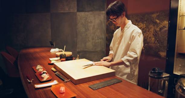 istock Japan chef, restaurant and knife for sushi and precision with sharp blade for gourmet fish menu in hotel. Asian man, hands and culinary artist on job by wood board, table and raw seafood on plate 1992930715