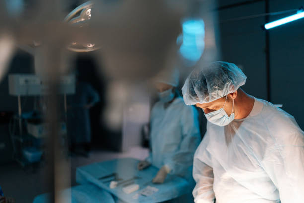 istock Selective focus of cooperating team of surgeons processing surgical operation in dark operating room modern hospital emergency department. 1992935943
