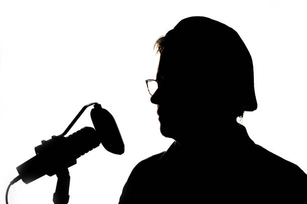 istock Voiceover artist silhouette in studio with microphone and hat on backwards 1992951778