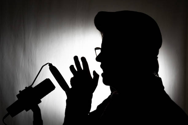 Voiceover artist silhouette in studio with microphone and pop filter wearing a hat against a black and white background
