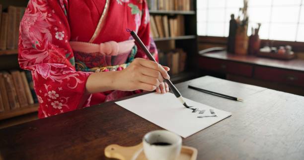 istock Hands, writing and Japanese woman for traditional script on paper, documents and letters in home. Creative, Asian culture and person with paintbrush tools for calligraphy, font and text in house 1993022796