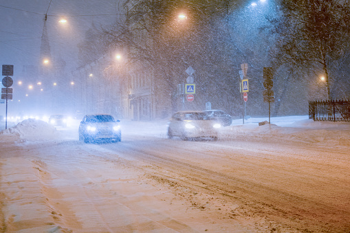 Cars driving along an evening winter city street during a snowstorm