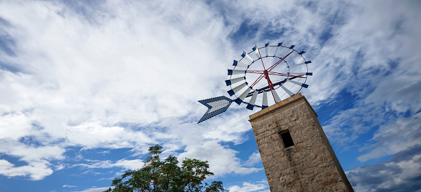 A traditional windmill reaches skyward, its sails contrasting with the dynamic textures of the sky