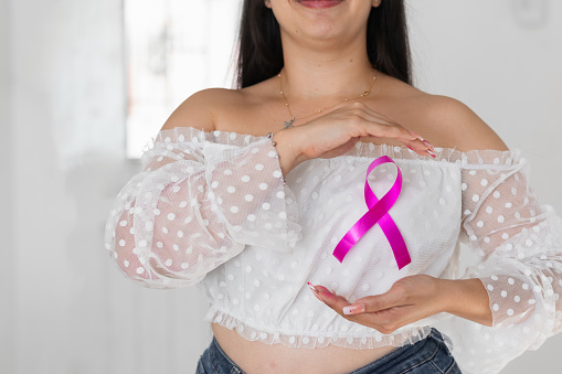 close-up of latina woman showing her pink ribbon, symbol of breast cancer, on her chest
