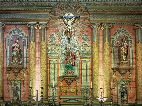 Santa Barbara, CA, USA - December 18, 2023: Colorful reredos with Jesus on the cross and Santa Barbara statue in Old Mission church. Others are Virgin Mary and Saint Joseph