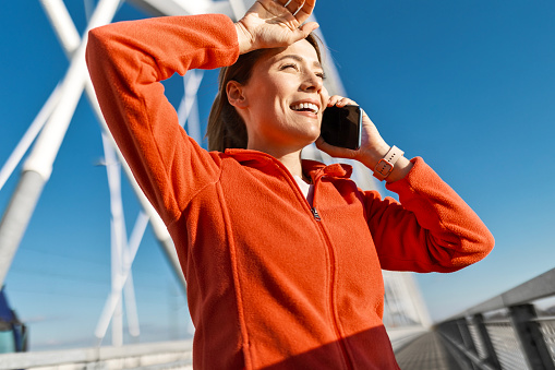 Happy sportswoman jogging at the bridge using smart phone