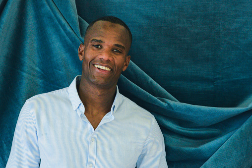 black young fit man smiling and standing over a blue velvet cloth
