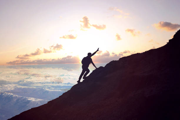 Silhouette of businessman climbing mountain on sunset